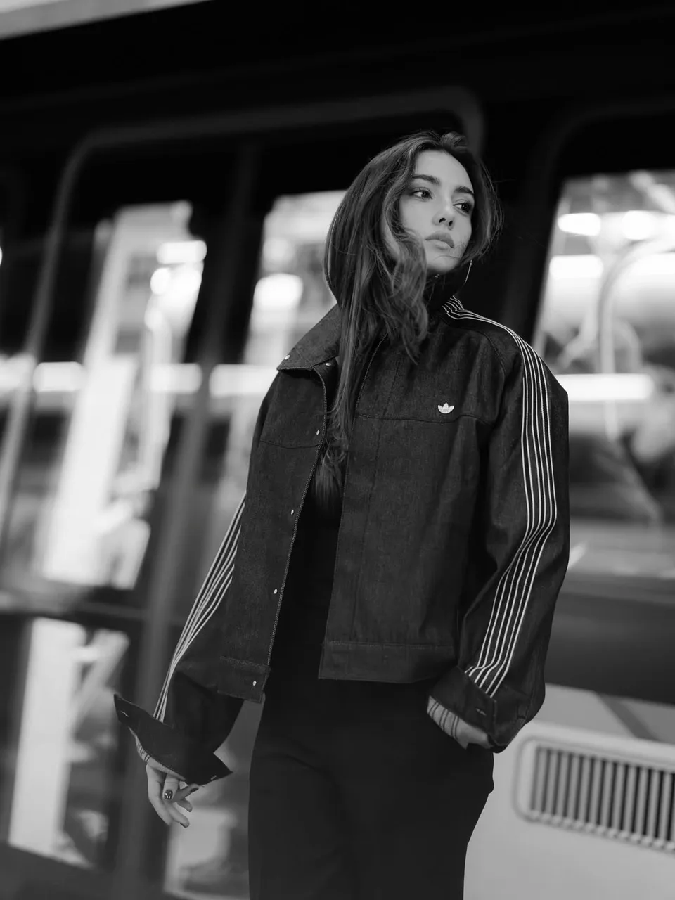 Zeudi en long manteau sombre sur un quai de gare, photographiée en noir et blanc.
