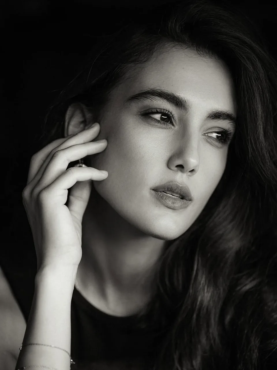 A black and white portrait of Zeudi looking aside with a hand beside her face.